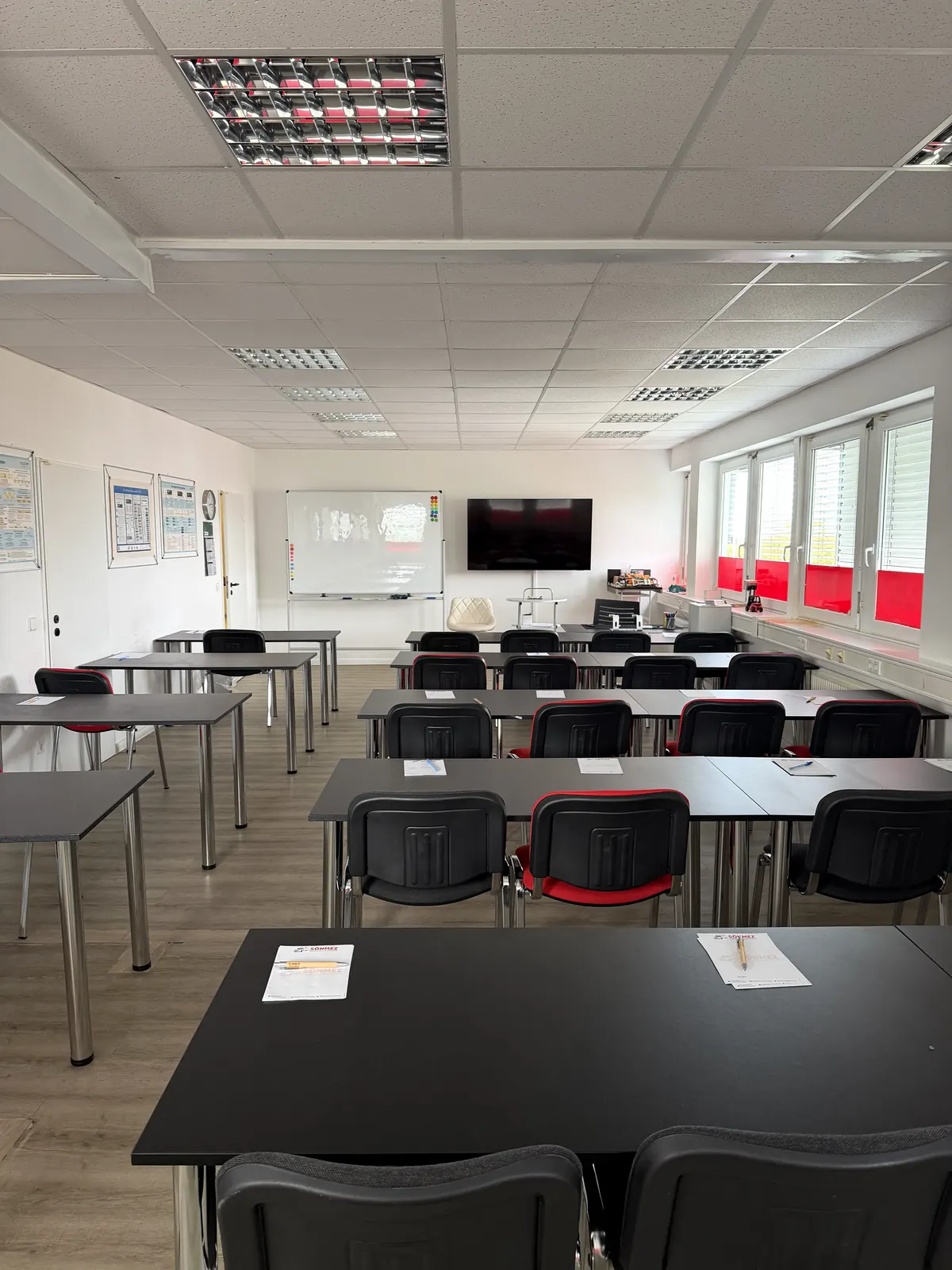 Schulraum mit Tischreihen, Whiteboard und großem Bildschirm